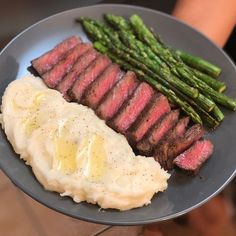 a plate with steak, mashed potatoes and asparagus on it is being held by a person