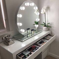 a mirror sitting on top of a white counter next to a flower pot and phone