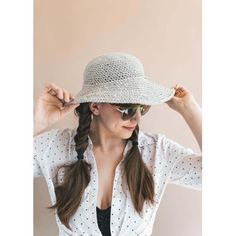 a woman wearing a hat and sunglasses is holding her hair in one hand while standing against a wall