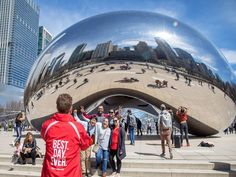 many people are standing in front of a large metal ball that is on top of some steps