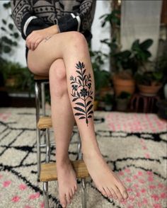 a woman sitting on top of a chair with her legs crossed and flowers tattooed on the leg