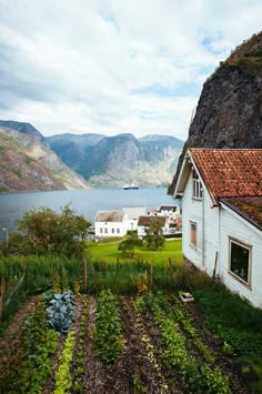 an old farm house sits on the edge of a lake with mountains in the background