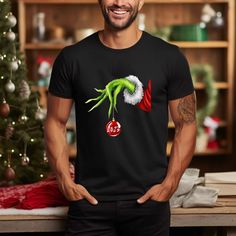 a man standing in front of a christmas tree wearing a grin face t - shirt