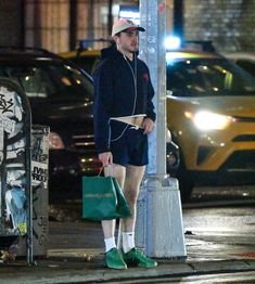 a man with headphones on standing next to a street pole and holding shopping bags