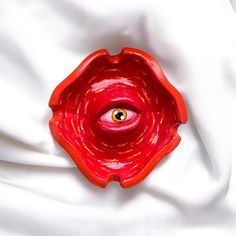 an eye is seen in the center of a red bowl on a white fabric background