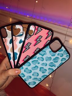 four cell phone cases with different designs on them in front of a pink wall and purple lights