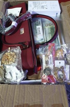 a red purse sitting on top of a cardboard box filled with jewelry and other items