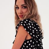 a woman in black and white polka dot dress looking at the camera with her hand on her hip