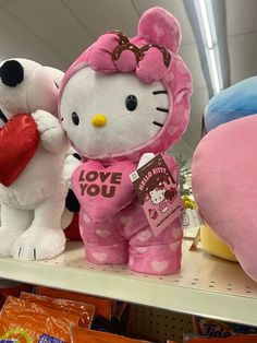 two hello kitty stuffed animals on a shelf in a store, one holding a heart