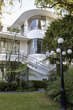 a tall white building sitting next to a lush green park filled with trees and plants