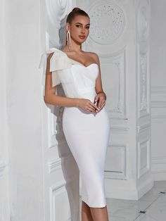 a woman in a white dress leaning against a wall with her hands on her hips