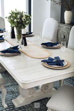 a dining room table with place settings and blue napkins on the placemat, along with flowers