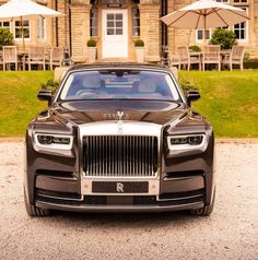 a black rolls royce parked in front of a house with umbrellas on the lawn