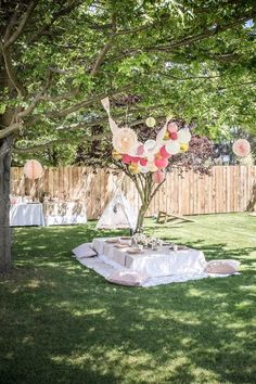 an outdoor party setup with balloons and paper flowers on the table in front of a wooden fence