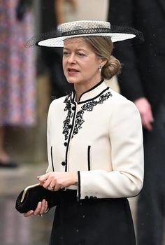 the queen is wearing a white hat with black trimmings and holding a purse