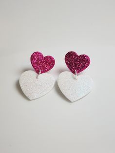 two white and pink heart shaped earrings sitting on top of each other's backs