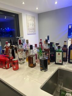 bottles of alcohol are lined up on the counter top in front of a sink and window