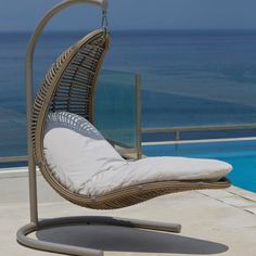 an outdoor swing chair next to a swimming pool with the ocean in the back ground