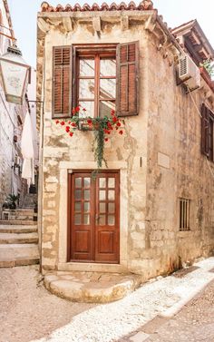 an old stone building with red flowers on the window sill and steps leading up to it