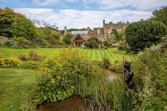 a pond in the middle of a lush green field next to a large stone building