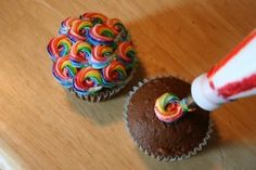 two cupcakes on a wooden table with a candy stick sticking out of them