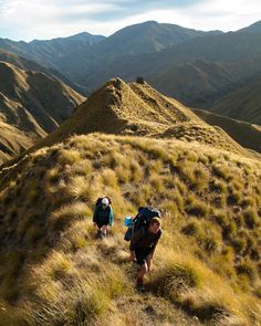 two people hiking up a hill in the mountains