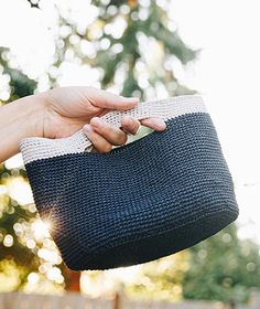 a hand holding a black and white purse in front of a fence with trees behind it