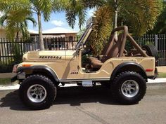 a tan jeep parked in front of a gated area with palm trees behind it