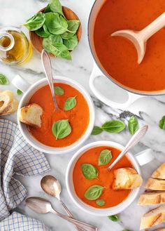 three bowls of tomato soup with basil leaves and bread on the side next to them