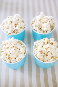 four blue bowls filled with popcorn sitting on top of a striped tablecloth covered table