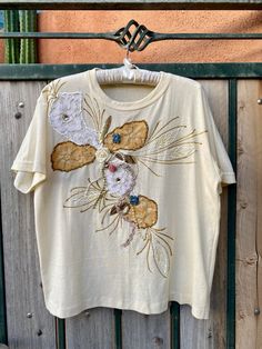 "Vintage 1980s - 1990s pale yellow women's t shirt. Beautifully embellished on front from its era with gold beads, pearls, lace flowers & leaves, ribbon florals, gold glitter outline, hand painted & more! Very shabby chic cute! No tags on this short sleeve T shirt that simply slips on overhead. Fits women size Large. Further measurements of: Shoulder to hem = 24\" Pit to pit = 22\" Waist = 21\" measured on 1 side when laying flat." Vintage Beige Short Sleeve T-shirt, Vintage Cream Short Sleeve T-shirt, Embellished Cotton Short Sleeve T-shirt, Cotton Embellished Short Sleeve T-shirt, Vintage Beige T-shirt, Embellished Graphic Tee With Short Sleeves, Vintage Cream Cotton Top, Embellished Graphic Tee With Crew Neck, Vintage Cream Embroidered Tops