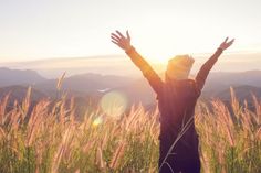 a person with their hands up in the air on top of a hill at sunset