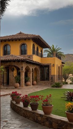 a large yellow house with many potted plants in front of it and a stone walkway leading to the entrance