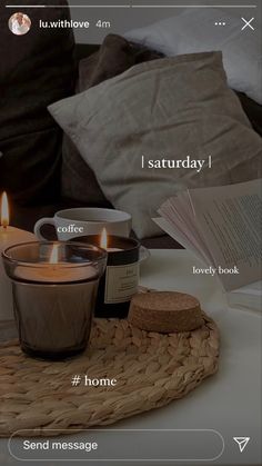 two candles sitting on top of a wicker tray next to a cup and book