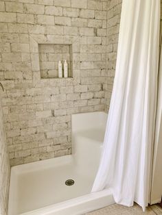 a white shower curtain in a bathroom next to a bathtub and toilet with a brick wall behind it