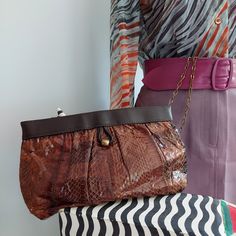 1970's Snakeskin. Savvy clutch/satchel. VINTAGE by Purse Strings, NY. Patchwork design of pieced snakeskins. The sleek shades of brown are versatile, adapt to wardrobes. Hinged sides, brass hardware. Chain bags debuted during the Disco Era, 1970's. On the dance floor, clutch bags swung easily by their chains. Roomy shape and size. Chain handle can stow away inside the bag. Brass bead and loop trim. Grosgrain fabric lining in walnut. Interior zip pocket. VINTAGE Width: 10" Height: 6.5" Vintage Brown Evening Bag For Party, Brown Party Clutch With Chain Strap, Vintage Brown Bag With Chain Strap, Vintage Brown Rectangular Evening Bag, Retro Brown Rectangular Clutch, Vintage Brown Party Bag, Vintage Brown Party Bags, Vintage Pouch Clutch For Everyday Use, Vintage Brown Evening Bag