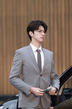 a man in a suit and tie standing next to a car with his hand on the door handle