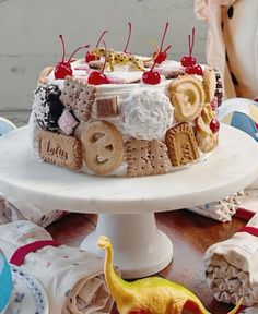 a birthday cake with cookies and candy on the top is decorated like a toy dinosaur