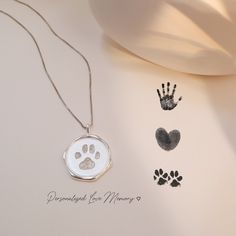 a dog paw and handprints on a white surface next to a silver necklace