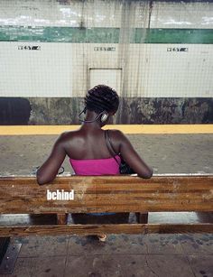 a woman sitting on top of a wooden bench next to a train platform with the word behind her