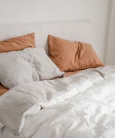 an unmade bed with white and brown pillows