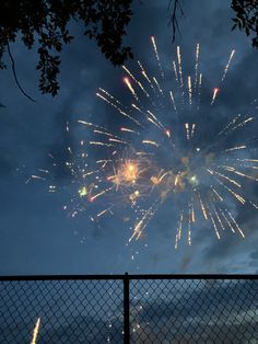 fireworks are lit up in the sky above a fence