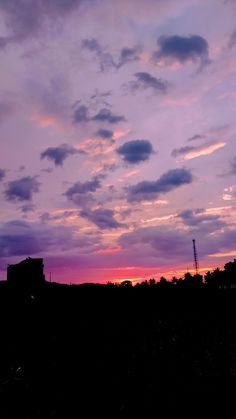 the sky is purple and pink as the sun sets in the distance with clouds above it