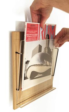 a person is holding up a magazine in front of a wooden frame that holds photos