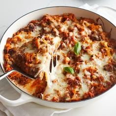 a casserole dish with meat and cheese being lifted from the pan by a spatula