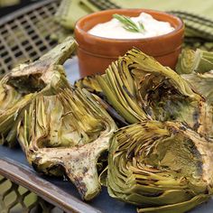 grilled artichokes on a plate with dip in a small bowl behind them