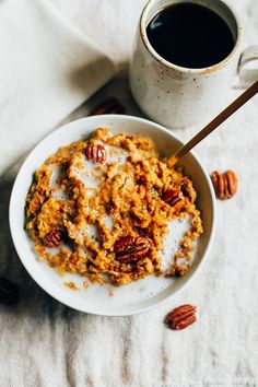 a bowl of oatmeal topped with pecans next to a cup of coffee