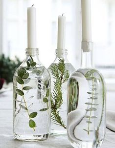 three glass bottles with plants in them sitting on a table next to candles and flowers