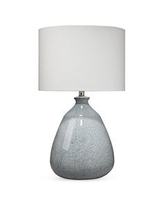 a gray table lamp with a white shade on the base and a light blue vase underneath it