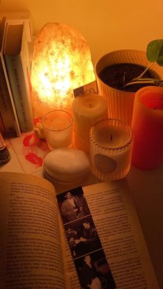 an open book sitting on top of a table next to two candles and some plants